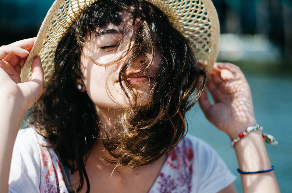 A woman wearing a straw hat and smiling pleasantly in a bright atmosphere signals sunburn.